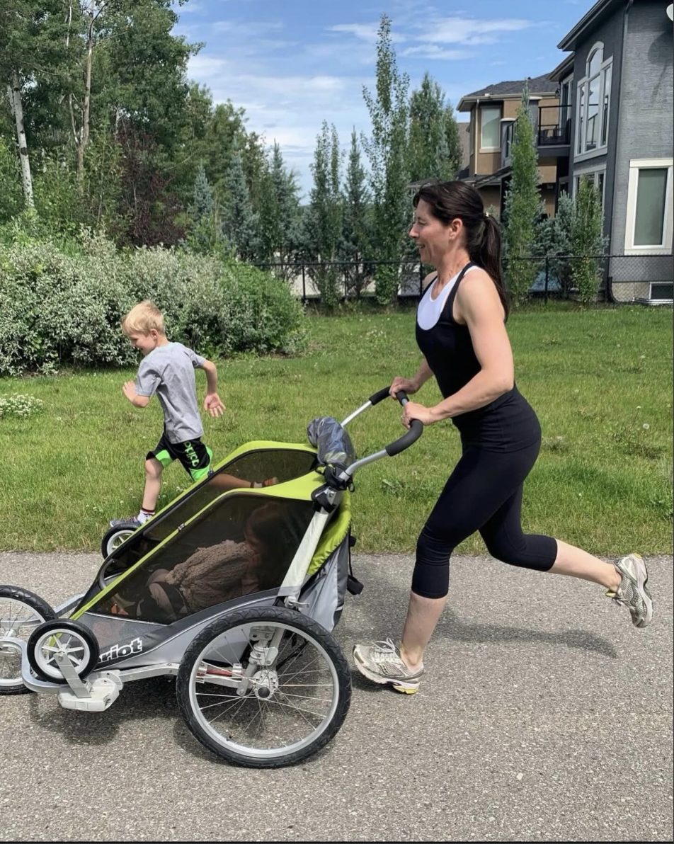 A mother running with a jogging stroller as her son races alongside