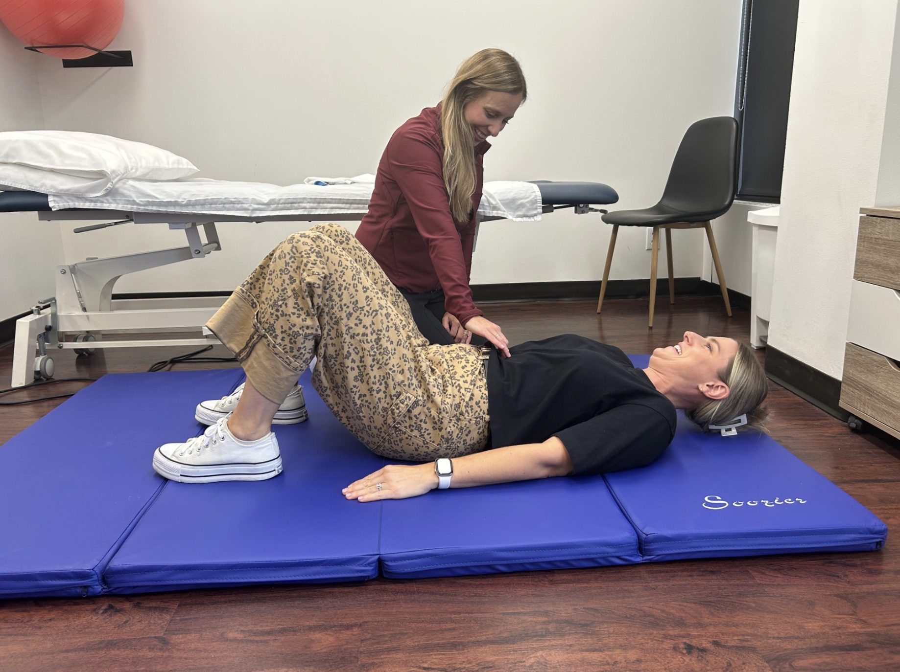 A physiotherapist guiding a client through core and pelvic floor activation on the mat